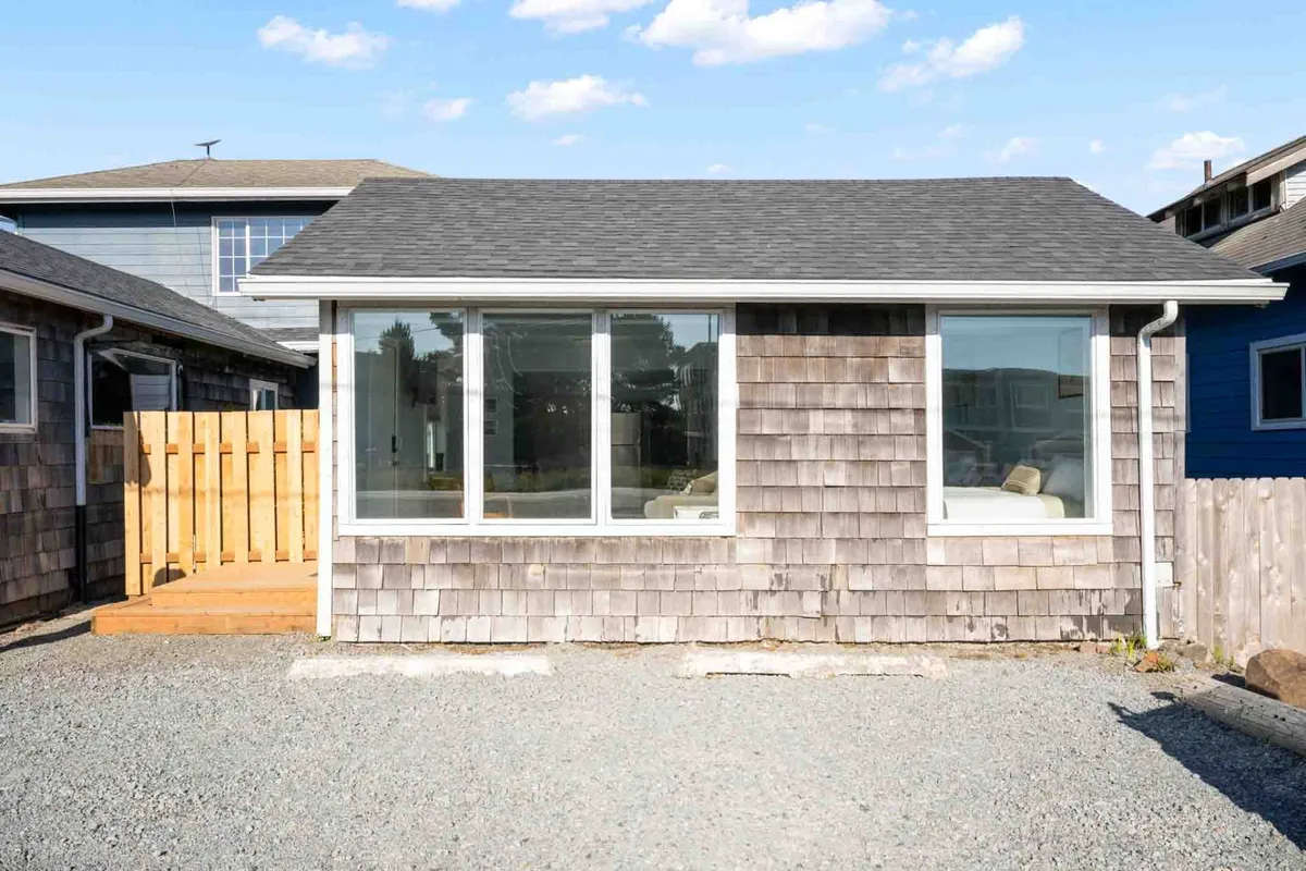 This image shows the exterior of the property, featuring large front windows, a welcoming wooden deck, and classic shingle siding. The scene evokes a sense of approachable comfort and emphasizes the cottage's connection to the outdoors.