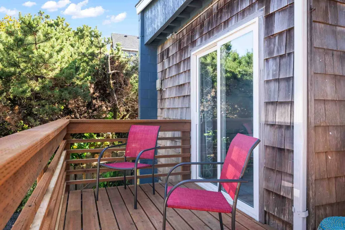 A comfortable wooden deck with two red chairs and a sliding glass door, blending indoor and outdoor living. The setup is inviting for morning coffee, quiet reflection, or sharing time with a pet in the fresh air.