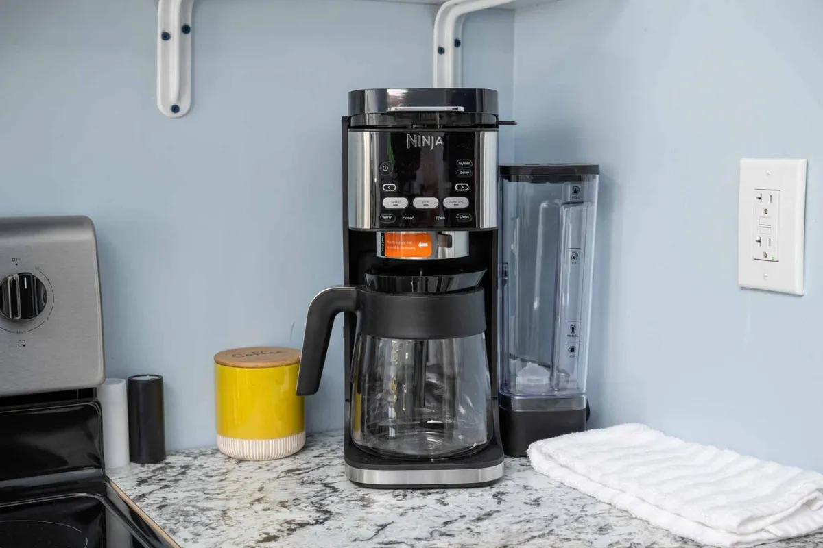A close-up of a granite countertop featuring a Ninja coffee maker and a yellow canister, evoking the comfort and practicality of preparing breakfast or coffee in the morning.