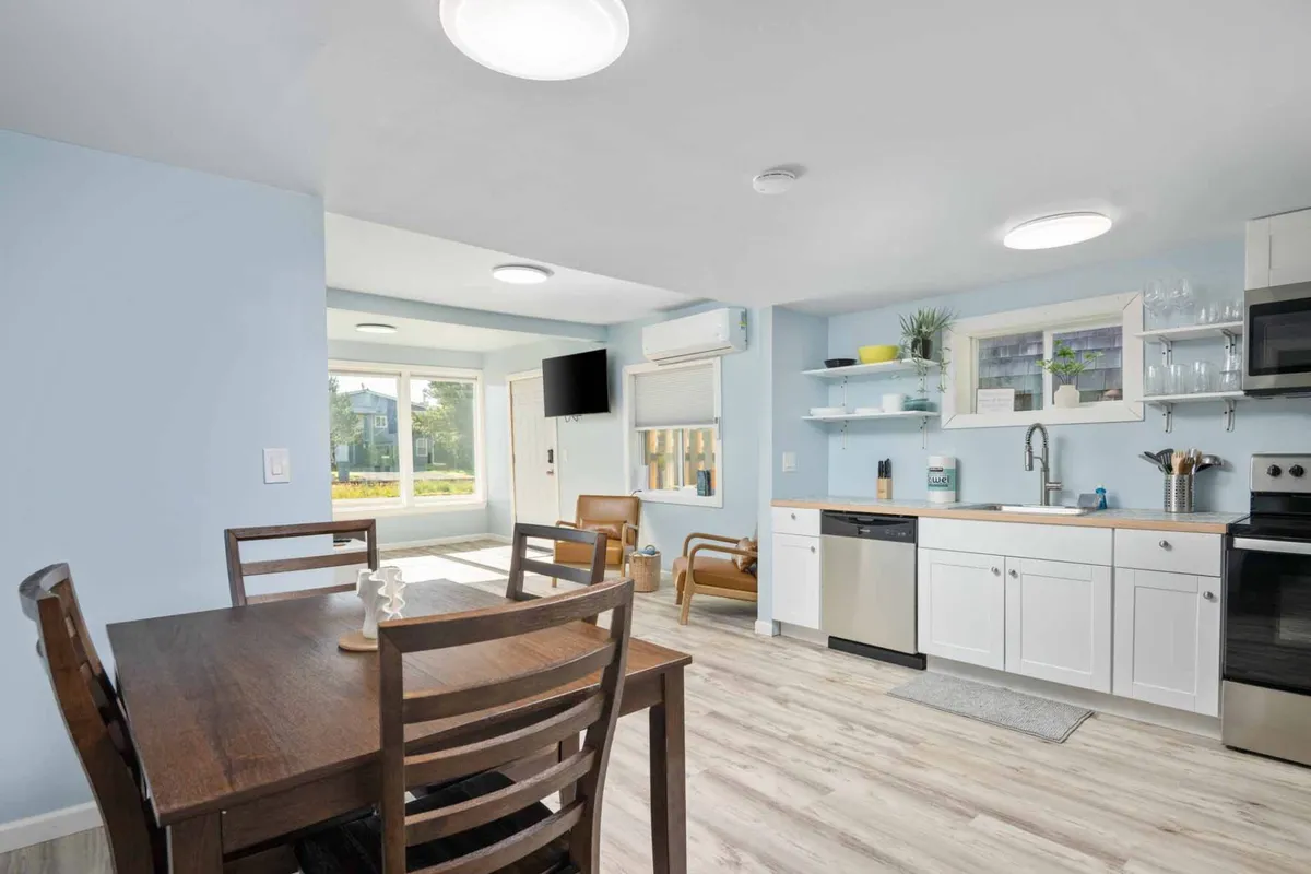 A welcoming dining area with a dining table, kitchen counter, large window letting in natural light, and a cozy seating area nearby. The layout encourages relaxed dining and social gatherings.