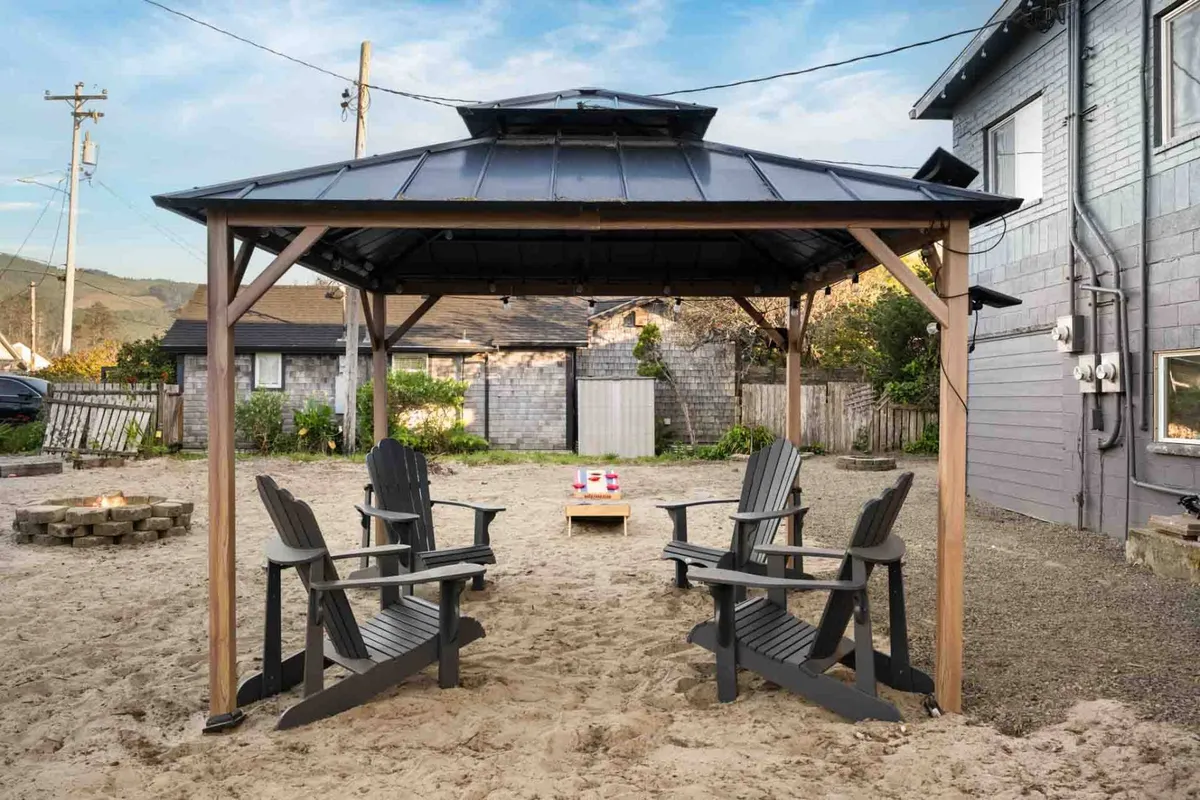 An exterior social area featuring a gazebo, classic Adirondack chairs, and a cozy fire pit. The arrangement is perfect for small-group conversations, enjoying s'mores, or simply relaxing by the fire as the sun sets.