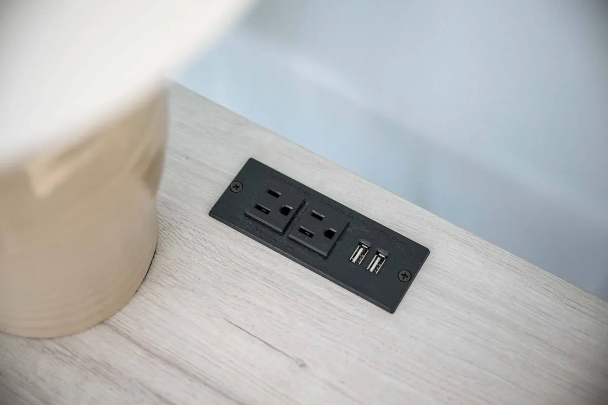 A close-up of a practical interior corner featuring an electrical outlet with USB ports and a decorative lamp, blending utility with comfort. This modern touch points to the space's suitability for working remotely.
